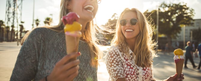 Zwei Frauen genießen einen Spaziergang im Sommerurlaub und essen ein Eis.