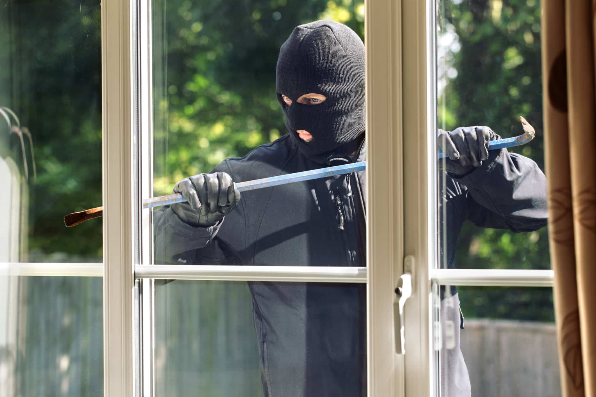 Einbrecher bricht mit einem Brecheisen durch ein Fenster in ein Haus ein.