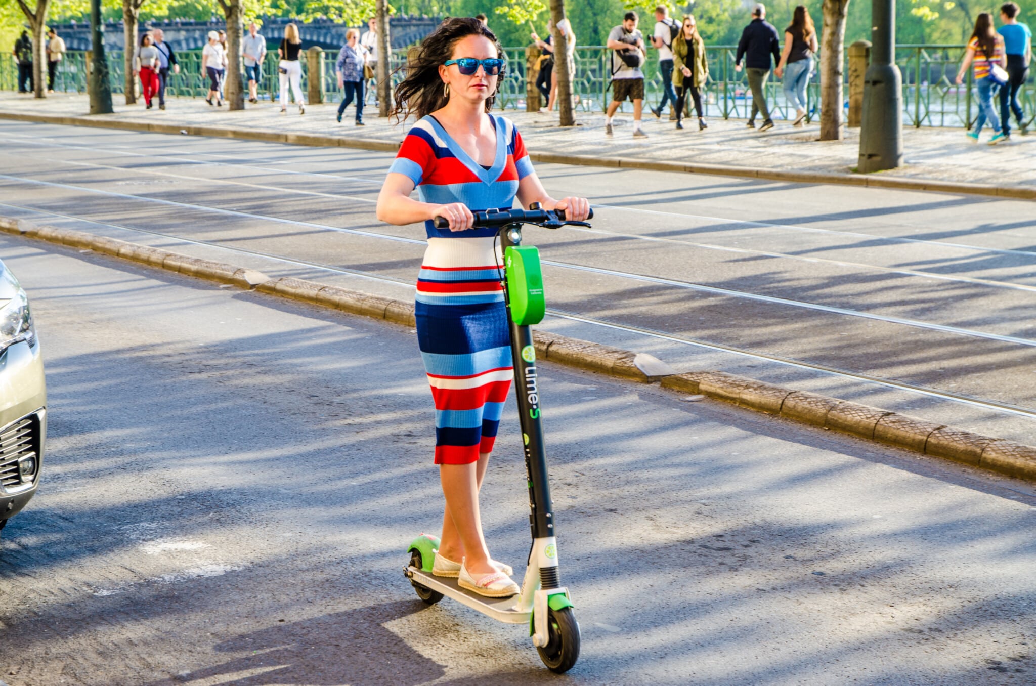 Frau in bunt-gestreiftem Kleid fährt auf E-Scooter durch die Innenstadt